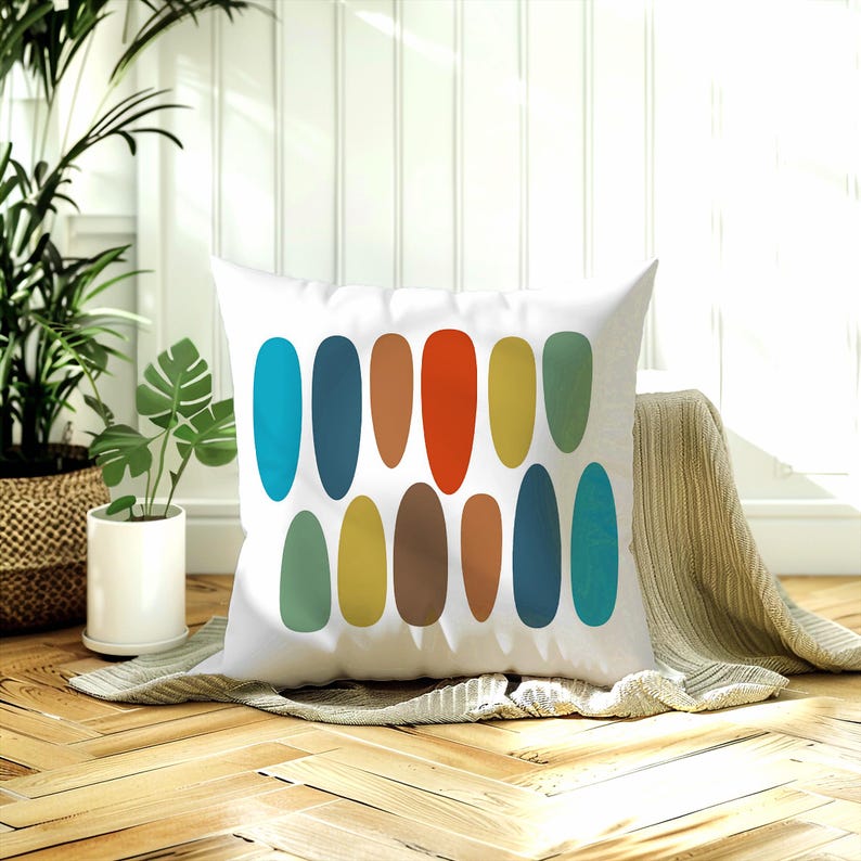 Mid-century oval throw pillow on a wood floor with a knit blanket, potted plants & sunlight streaming through a window.