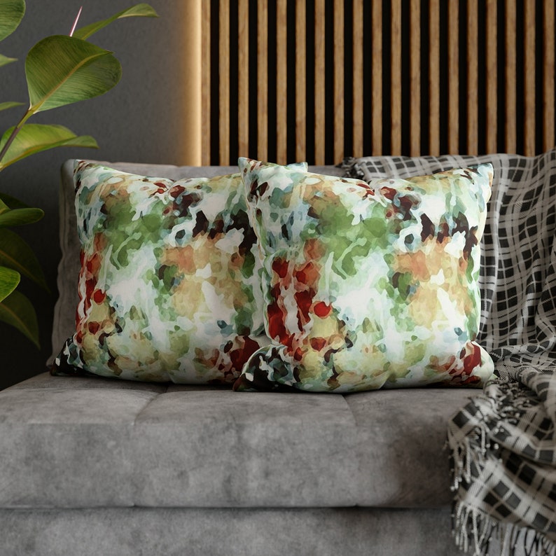 This image shows two square throw pillows with an abstract floral design. The modern impressionist design features brushstrokes of green, brown, & red watercolor paint resembling branches, leaves, & petals.