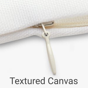 Close-up of a blank, white, textured canvas pillow cover with a hidden zipper, highlighting durable weave & neat stitching.