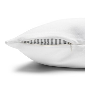 Close-up of a white pillow’s side concealed zipper, showing a gray & white striped inner insert against a white background.