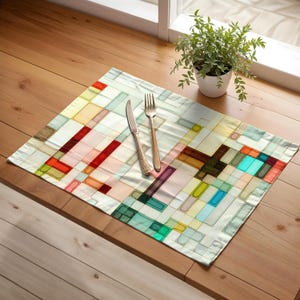 May include: A rectangular placemat with a colorful geometric pattern in shades of red, green, blue, and brown. A fork and knife with ornate handles rest on the placemat. A small potted plant sits in the background.