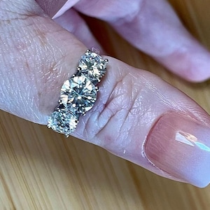 May include: A silver ring with four large, round, clear gemstones. The ring is on a person's finger.