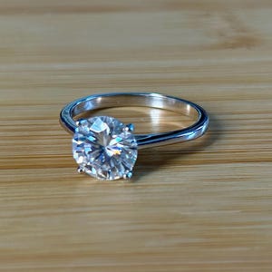 Moissanite solitaire. A lovely 3ct certified round brilliant Moissanite in a cathedral-style setting, with 4 prongs and a sleek plain band!