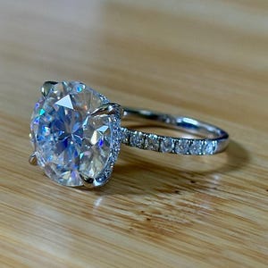 May include: A silver ring with a large, round, clear gemstone as the centerpiece. The band is also adorned with smaller, clear gemstones. The ring is set against a wooden surface.