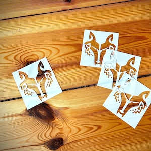 Könnte beinhalten: Vier weiße Papierschablonen mit einem Wolfskopfdesign, auf einer Holzoberfläche angeordnet.