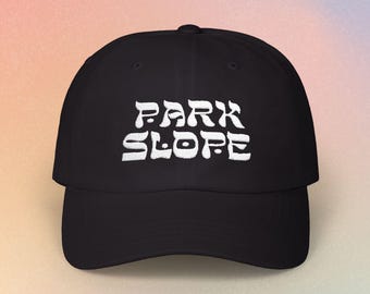 May include: A black baseball cap featuring the white embroidered text PARK SLOPE on the front. The cap has a structured crown, a curved brim, and a button on the top center. The embroidery uses a stylized, bold font for the lettering.