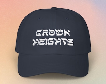 May include: A navy blue baseball cap featuring the white embroidered text Crown Heights in a stylized font across the front panel. The cap has a structured crown, a curved brim, and a button at the top center of the headwear piece.