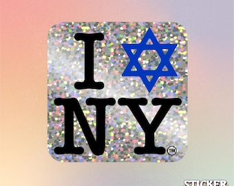 May include: A square sticker with a holographic, multi-colored glitter finish. The design features the black text I, a blue Star of David, and the black text NY with a small trademark symbol in the bottom right corner of the sticker.