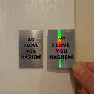 Può includere: Due magneti rettangolari in metallo con la scritta "SAY I LOVE YOU HASHEM!". Un magnete è argentato con una texture spazzolata, l'altro è olografico con una lucentezza arcobaleno.