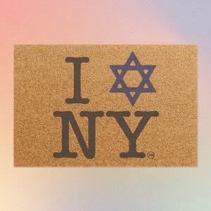 Op de afbeelding: Een rechthoekige deurmat van natuurlijke vezels. De mat heeft de tekst "I NY" in donkerbruine letters, met een blauwe Davidster die de "O" vervangt. Het handelsmerksymbool staat in de rechter benedenhoek.