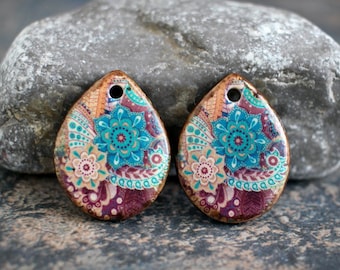 Puede incluir: Dos colgantes de cerámica en forma de lágrima con un diseño paisley colorido. Los colgantes son una mezcla de colores turquesa, marrón, blanco y rosa. Cada colgante tiene un agujero en la parte superior para encordar.