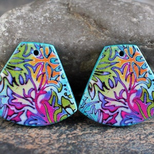 以下が含まれることがあります： ピンク、パープル、グリーン、オレンジ、ブルーの色の花柄が施された、カラフルな三角形のポリマークレイのイヤリングが2つ。イヤリングはターコイズブルーの背景に、フック用の穴が開いています。