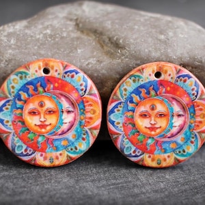 May include: Two round, colorful wooden pendants with a sun and moon design. The sun and moon have faces and are surrounded by a colorful mandala pattern.