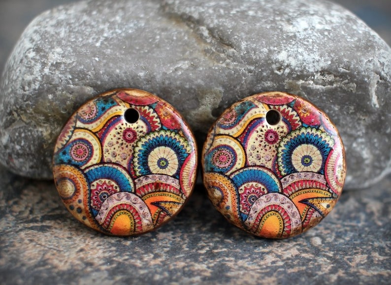 Puede incluir: Dos colgantes redondos de madera con un dise&ntilde;o paisley colorido. Los colgantes tienen un agujero en el centro para encordar.