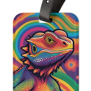 May include: A colorful luggage tag featuring a vibrant, rainbow-colored lizard with a psychedelic background. The lizard has a bright orange body with purple, blue, and green accents. The background is a swirling pattern of rainbow colors.
