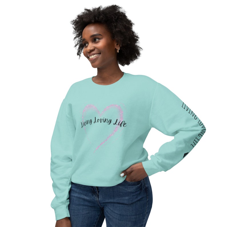 May include: A turquoise blue sweatshirt with a pink glitter heart and the text "Living Loving Life" on the front. The text is repeated on the sleeve.