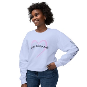 May include: A light blue sweatshirt with a pink heart and the text "Living Loving Life" on the front. The text "Living Loving Life" is repeated on the sleeves.
