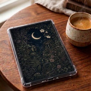 Op de afbeelding: Een doorzichtige beschermhoes voor een tablet met een donkere, gedetailleerde illustratie van een tuin bij nacht en maanlicht. Het ontwerp toont een maansikkel, dicht gebladerte, varens, bloeiende bloemen en architecturale elementen in zwart en goud.