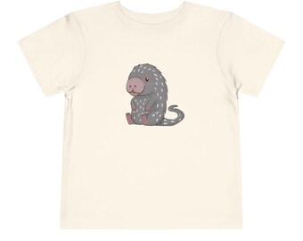 May include: A white toddler t-shirt with a cartoon illustration of a gray and white spiky animal with a pink nose.