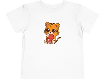 May include: White toddler t-shirt with a cartoon illustration of an orange and black tiger cub wearing a pink bow and holding a red steak.