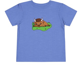 May include: A blue toddler t-shirt with a cartoon illustration of a brown bison lying down on green grass.