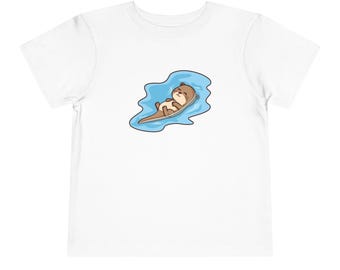 May include: White toddler t-shirt featuring a cartoon otter floating on its back in blue water. The otter is brown with a cream-colored belly and is smiling. The t-shirt is made of a soft, comfortable material.