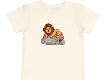 May include: A white t-shirt with a cartoon illustration of a lion sitting on a rock. The lion is brown and orange with a brown mane. The rock is gray.