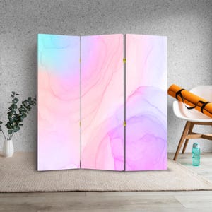Op de afbeelding: Een driedelige roomdivider met een abstract aquarelontwerp in roze, paars en blauw. De divider is gemaakt van hout en heeft een licht houten frame.
