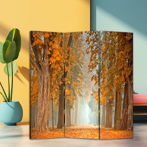 May include: A three-panel room divider depicting an autumnal forest scene. The image shows tall trees with golden leaves, a path strewn with fallen leaves, and a misty, sunlit background. The divider brings a natural aesthetic to any space.