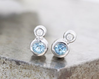 May include: A pair of silver stud earrings with a small round diamond and a larger round blue topaz stone.