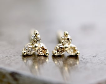 May include: A pair of gold earrings with three small diamonds each, set in a triangular shape.