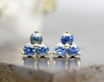 May include: A pair of gold stud earrings with three blue sapphires each, arranged in a triangular shape.