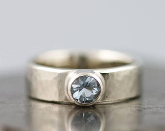 May include: A silver band ring with a light blue gemstone set in the centre.