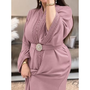 May include: A dusty rose long-sleeved dress featuring intricate vertical embroidery along the center front and sleeve cuffs. The garment includes a matching belt cinched at the waist with a large, circular, pearl-encrusted decorative buckle.