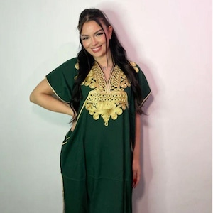May include: A dark green kaftan dress featuring short sleeves and a V-neckline. The garment is adorned with intricate gold embroidery around the neckline and chest area, with gold trim detailing along the sleeves and side seams of the dress.
