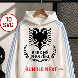 May include: A white hoodie featuring a black double-headed eagle emblem above the text BËRË NË SHQIPËRI, framed by a laurel wreath. The sleeves have three light blue stripes. Text in red circles reads 10 SVG and BUNDLE NEXT ->.
