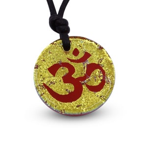 May include: A gold and red glass pendant necklace with the Om symbol. The pendant is round and has a textured surface. The necklace is made of black cord.