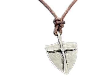May include: A silver shield pendant with a cross design hangs from a brown leather cord.