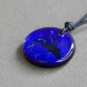 May include: A blue glass pendant with a black hummingbird silhouette, hanging from a black leather cord.