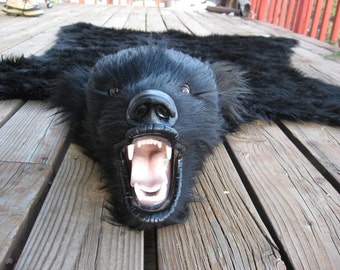 May include: Black bear rug with a snarling face and open mouth. The rug is made of real fur and has a realistic appearance.