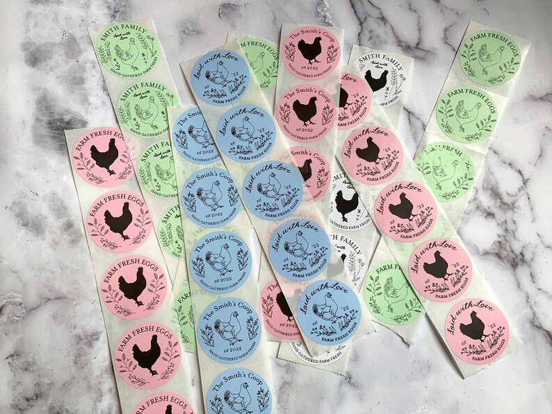May include: A collection of round stickers with various designs. Some stickers feature a black silhouette of a chicken, while others display a chicken illustration. The stickers are in pink, blue, and green, with text such as "Farm Fresh Eggs" and "Laid with Love."