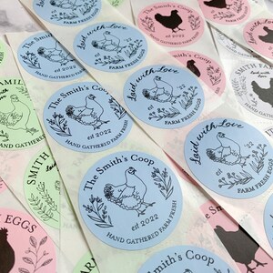 May include: A collection of round stickers with various designs. The stickers feature illustrations of chickens, floral elements, and text such as "The Smith's Coop", "Laid with Love", and "Hand Gathered Farm Fresh Eggs". The color palette includes blue, pink, and green.