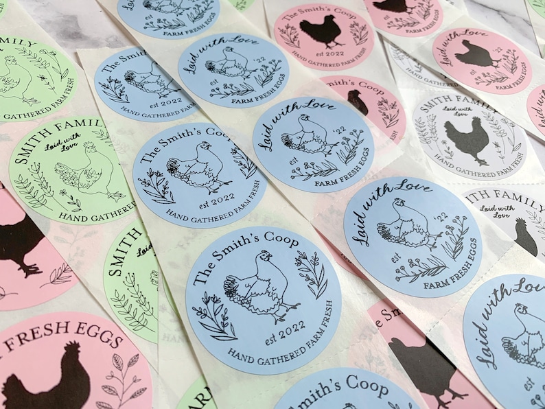 May include: A collection of round stickers with various designs. The stickers feature illustrations of chickens, floral elements, and text such as "The Smith's Coop", "Laid with Love", and "Hand Gathered Farm Fresh Eggs". The color palette includes blue, pink, and green.