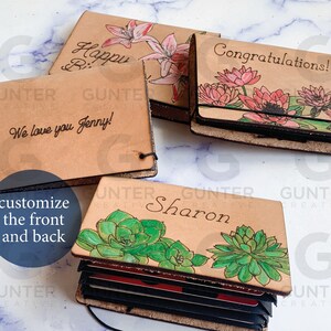May include: Four leather card holders with different designs. The first has a floral design with the text "Happy Birthday". The second has a floral design with the text "Congratulations!". The third has a succulent design with the text "Sharon". The fourth has a floral design with the text "We love you Jenny!"