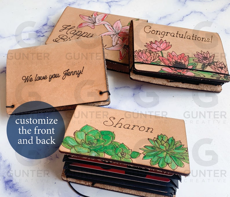 May include: Four leather card holders with different designs. The first has a floral design with the text "Happy Birthday". The second has a floral design with the text "Congratulations!". The third has a succulent design with the text "Sharon". The fourth has a floral design with the text "We love you Jenny!"