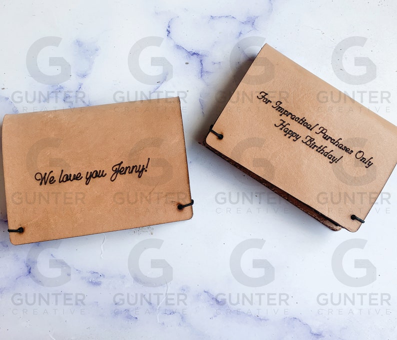 May include: Two brown leather wallets with engraved text. The first wallet says "We love you Jenny!" The second wallet says "For Impractical Purchases Only Happy Birthday!"