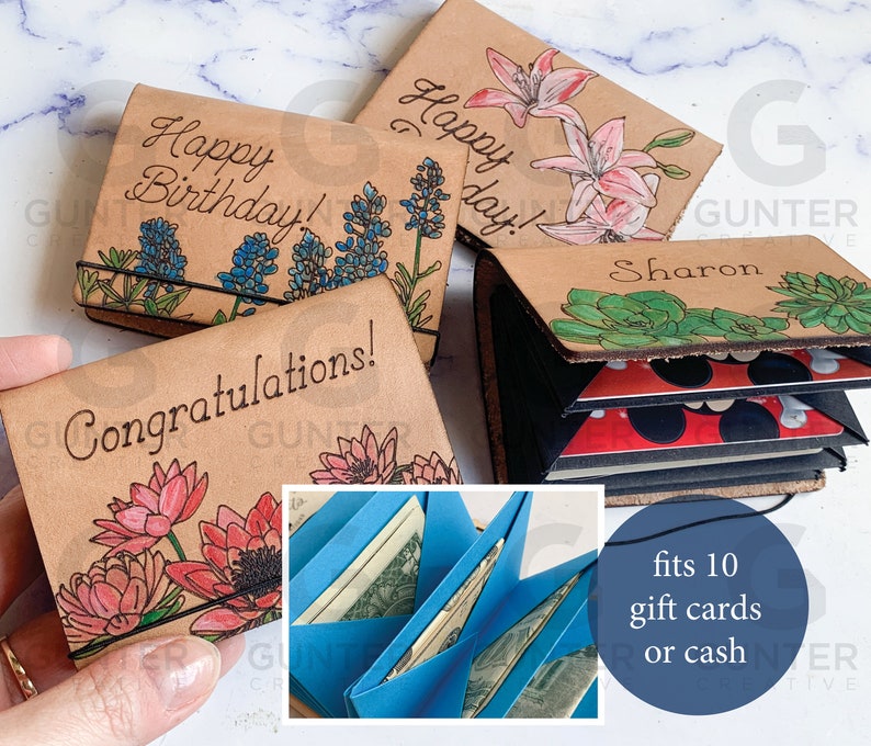 May include: Four leather gift card holders with different floral designs. The holders are open to show the blue card slots inside. The text on the holders reads "Happy Birthday!", "Happy Day!", "Congratulations!" and "Sharon". The text "fits 10 gift cards or cash" is also visible.