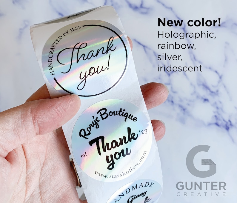 May include: Holographic, rainbow, and iridescent stickers with the words "Thank you!" and "Rory's Boutique" printed on them. The stickers are round and have a shiny, reflective surface. The text "New color!" is also visible.