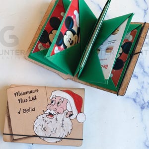 May include: Handmade leather journal with green pockets holding cards featuring Mickey Mouse. A second journal with a Santa Claus illustration and the text "Mawmaw's Nice List" is also shown.