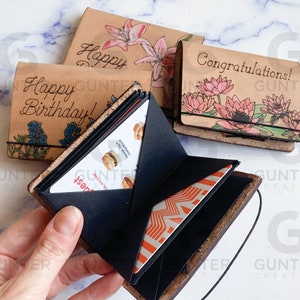 May include: A set of three leather-bound journals with floral designs and personalized messages. The journals are open to reveal a black gift card holder with a gift card inside.